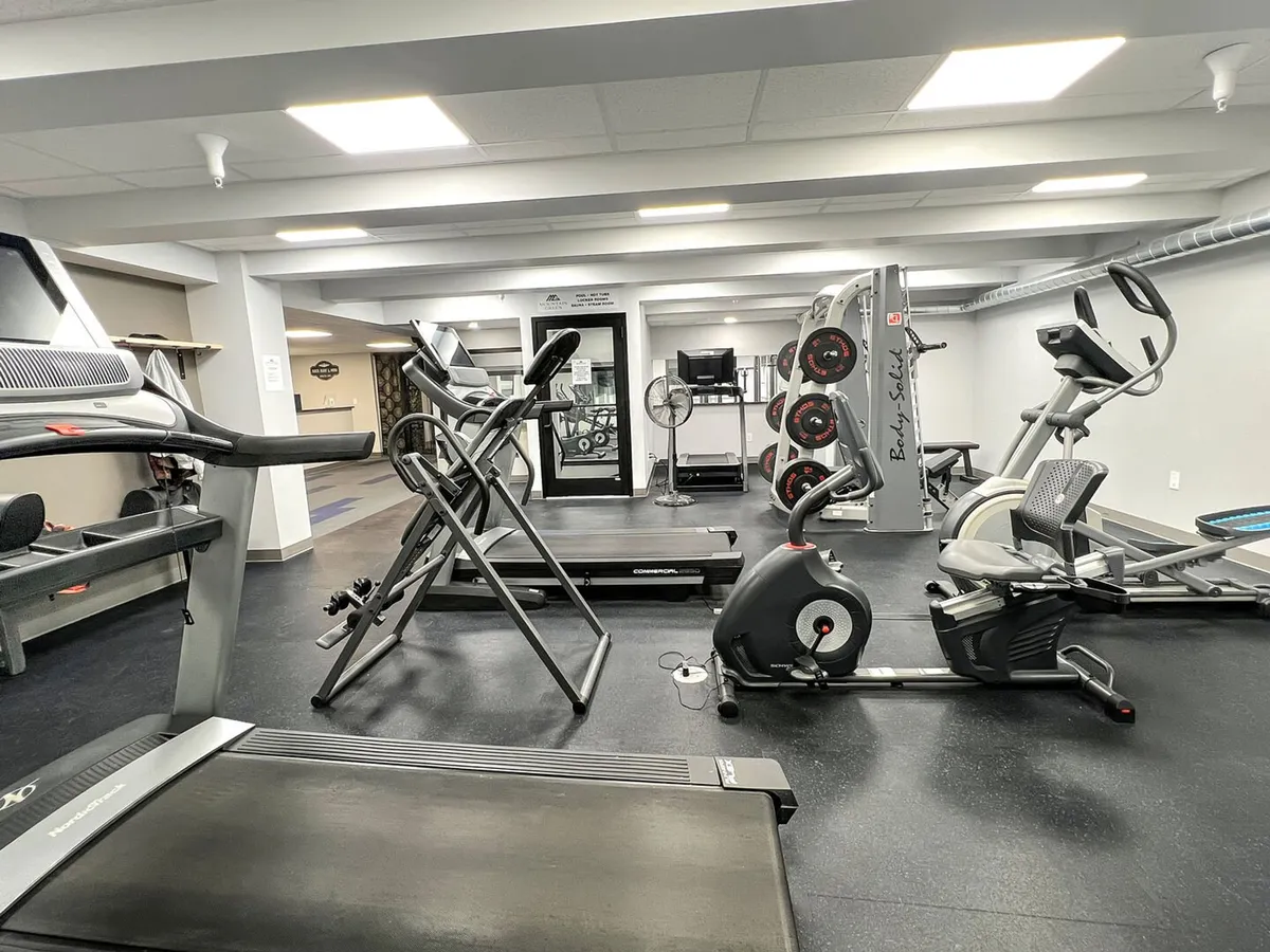 A motivating view of the fitness center’s interior, equipped with treadmills, elliptical machines, weight lifting equipment, televisions, and fans. The energetic environment suggests opportunities for both solo workouts and group fitness activities, echoing the section’s emphasis on health and activity.