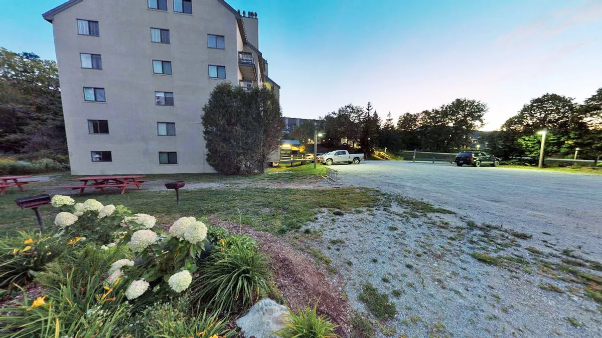 This exterior view showcases the building’s inviting facade, surrounded by flower beds, a well-maintained parking area, and mature trees. The outdoor setting hints at relaxation and gathering spaces, while the parking area implies easy access for guests on the go.