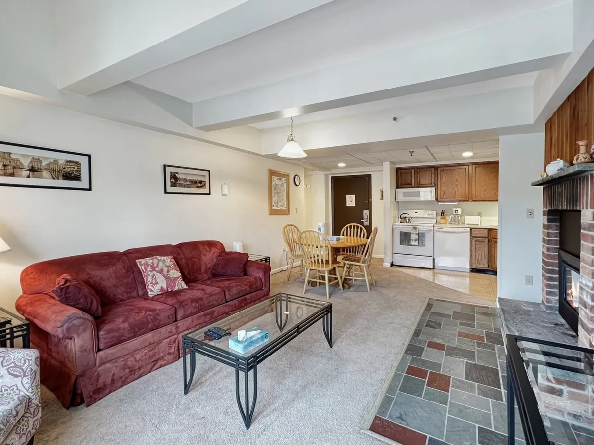 The image showcases a warm, inviting living space featuring a striking red couch, a sleek glass coffee table, an adjacent dining area perfect for shared meals, and a well-equipped open kitchen. The atmosphere is cozy, suggesting comfort and relaxation for families or groups after a day on the slopes or golf course.