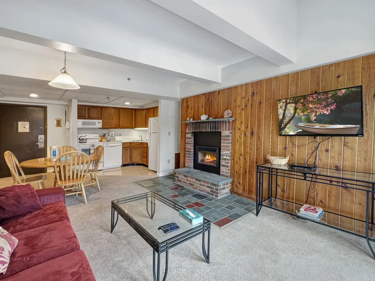 The image showcases a stylish and inviting living and dining area anchored by a fireplace, with a dining table set for gathering, a comfortable sofa, and a TV on the wall. Ambient lighting and warm finishes create a space ideal for relaxing after a day outdoors.