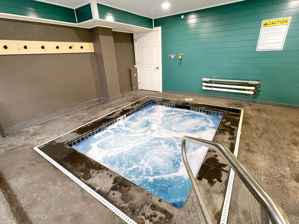 A tranquil indoor jacuzzi with softly bubbling water, set against a bright teal wall and a calming atmosphere. The space suggests a soothing post-adventure retreat, ideal for unwinding after a day on the mountain.